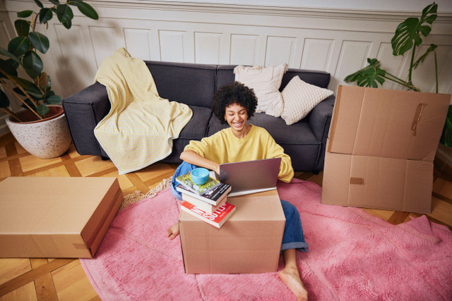 Une jeune femme qui utilise un ordinateur portable sur un carton de déménagement