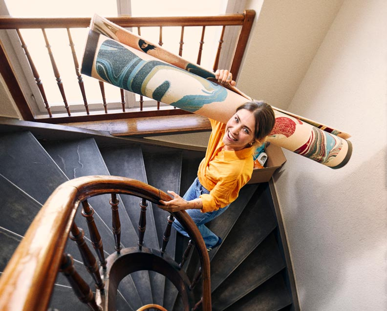 Une jeune femme qui monte les escaliers avec un tapis sur l'épaule