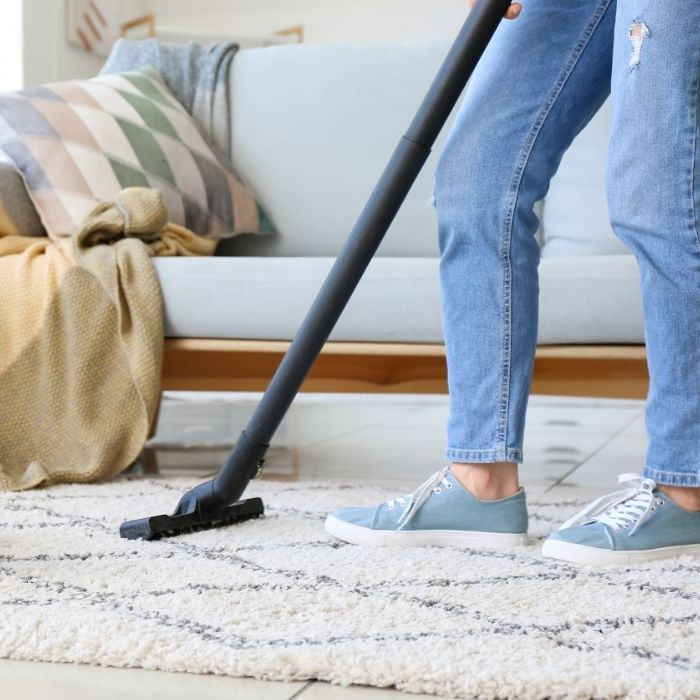 Eine Person saugt ihren Wohnzimmerteppich, auf dem ihr Hund liegt.