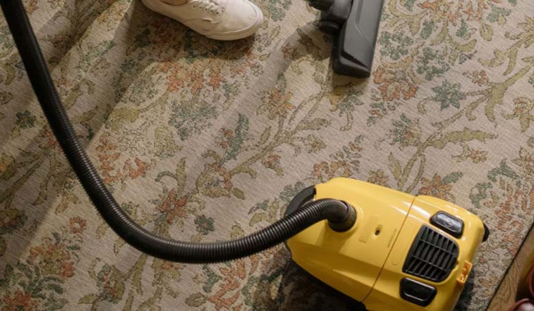 Una persona che pulisce il proprio tappeto con un aspirapolvere