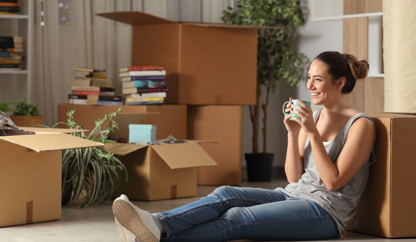 Eine entspannte junge Frau sitzt mit Umzugskartons auf dem Boden