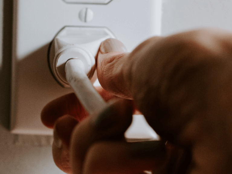 Geste de la main qui débranche une prise électrique pour réduire la consommation d’énergie