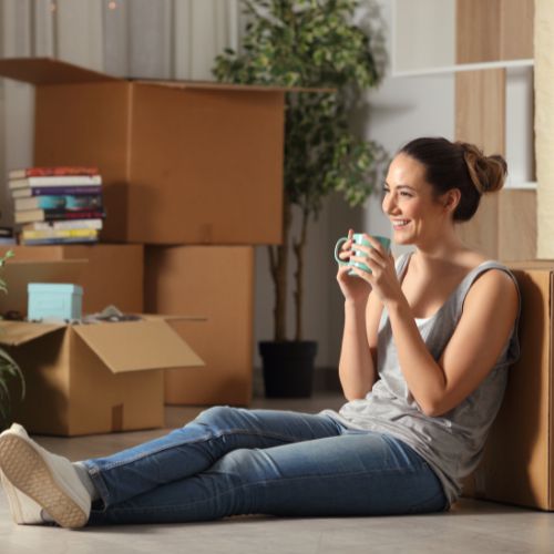 Una giovane donna rilassata siede sul pavimento con alcuni scatoloni da trasloco